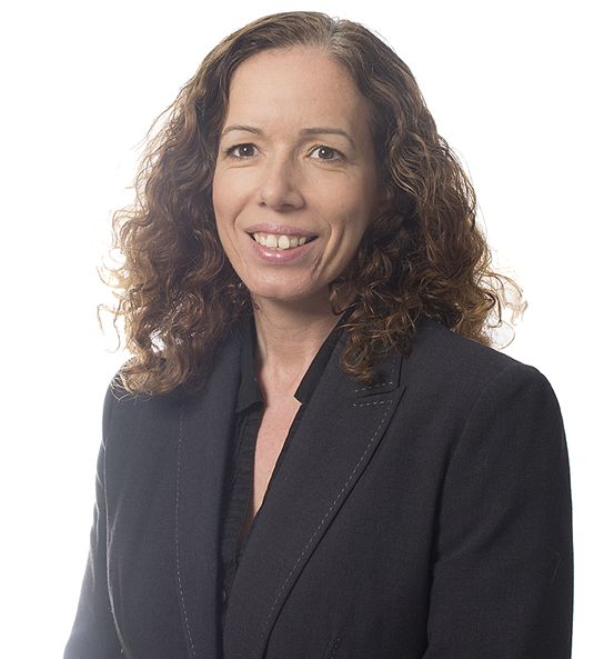 A woman with curly hair wearing a dark blazer, smiling at the camera in a professional setting.