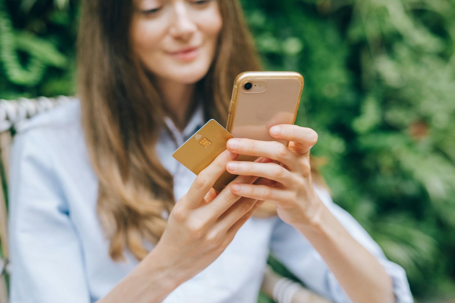 A woman with long hair holding a smartphone in one hand and a credit card in the other hand.