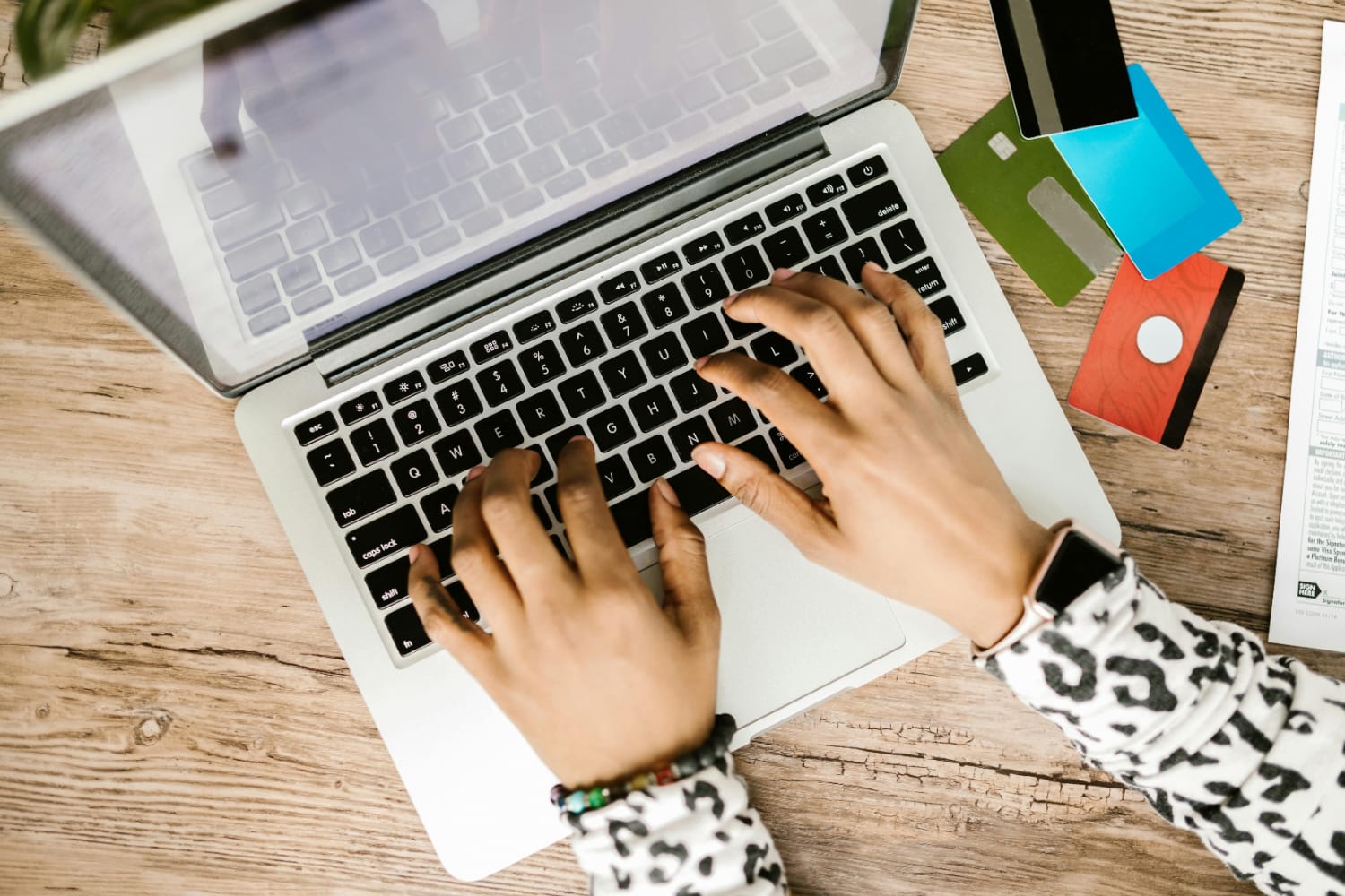 Hands typing on a MacBook keyboard with several credit cards visible on the table.