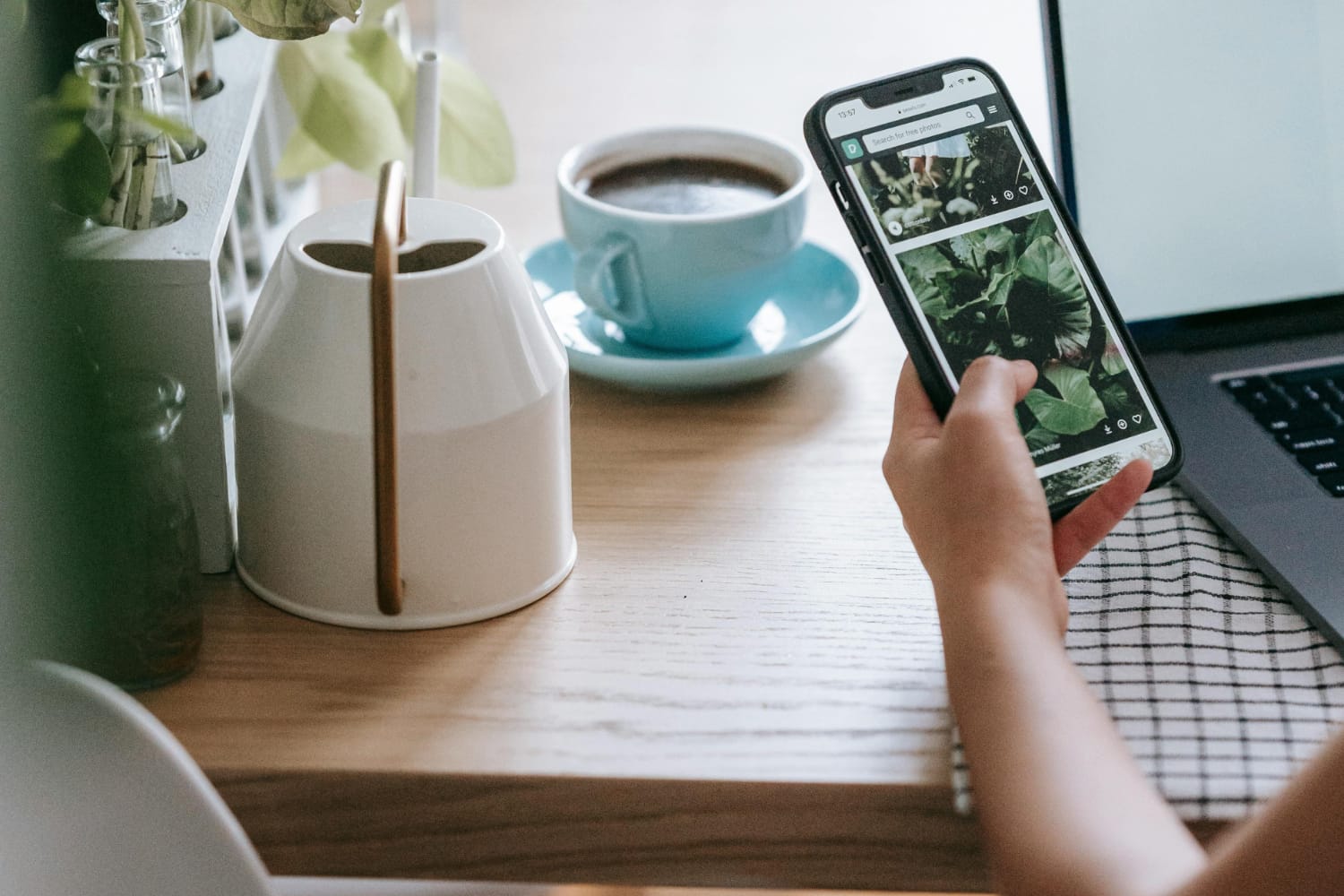 A smartphone displaying images of plants next to a blue coffee cup on a wooden table.