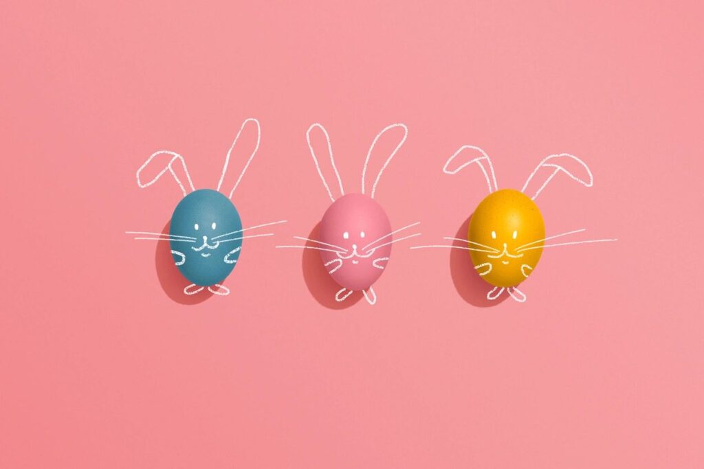 Three decorated Easter eggs in blue, pink, and yellow with bunny features drawn on a pink background.