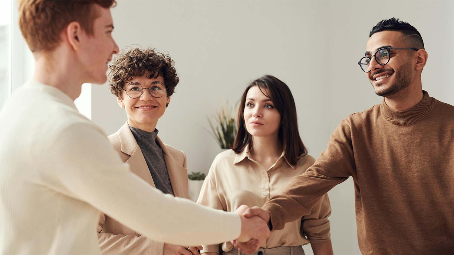 Two individuals shaking hands during a business meeting with two others observing.