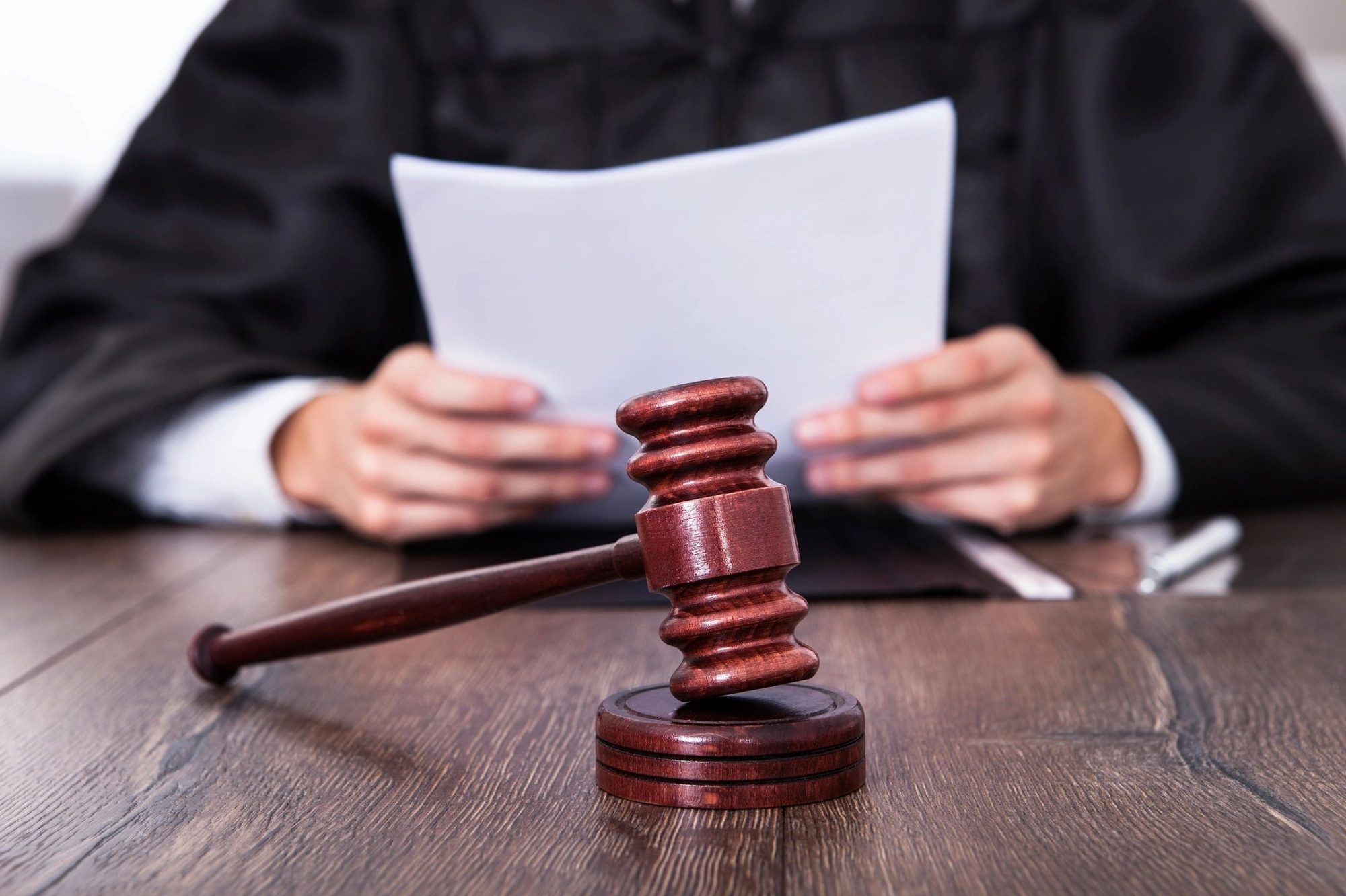 A wooden gavel placed on a table in front of a judge holding legal documents.